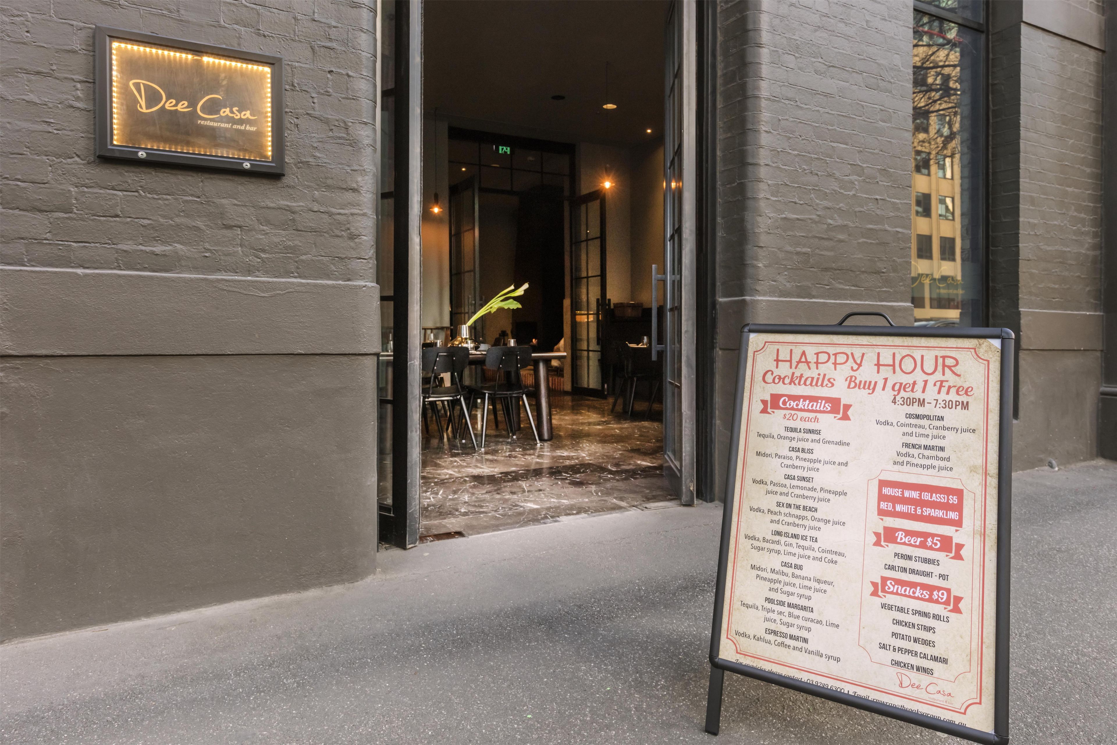 Ein Restaurant-Eingang mit einem Schild, das Happy-Hour-Angebote auflistet.