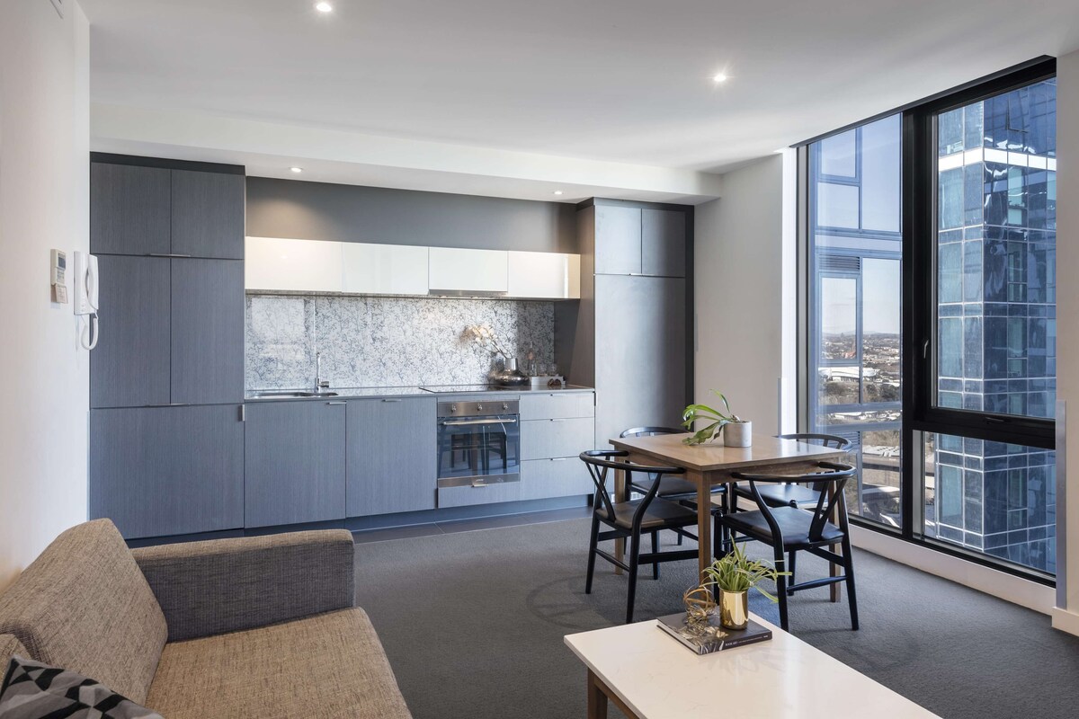 A modern kitchen with grey cabinets, a marble backsplash, and a dining area with a table and chairs.