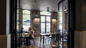 An interior with tables and chairs, large windows, and a brick wall. - WRAP on Southbank (Southbank)
