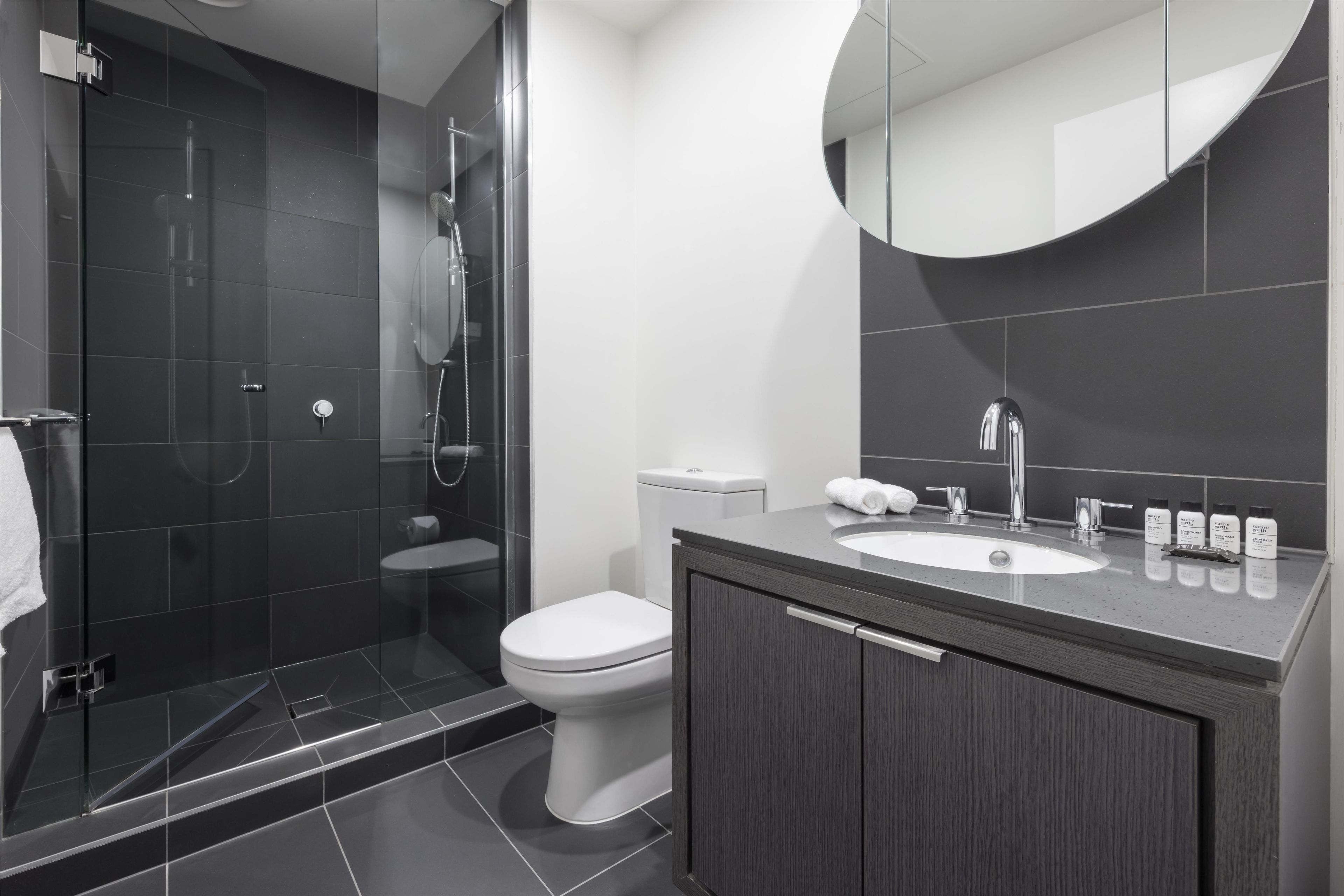 A modern bathroom with a glass-enclosed shower, a toilet, and a vanity with a sink and mirror.