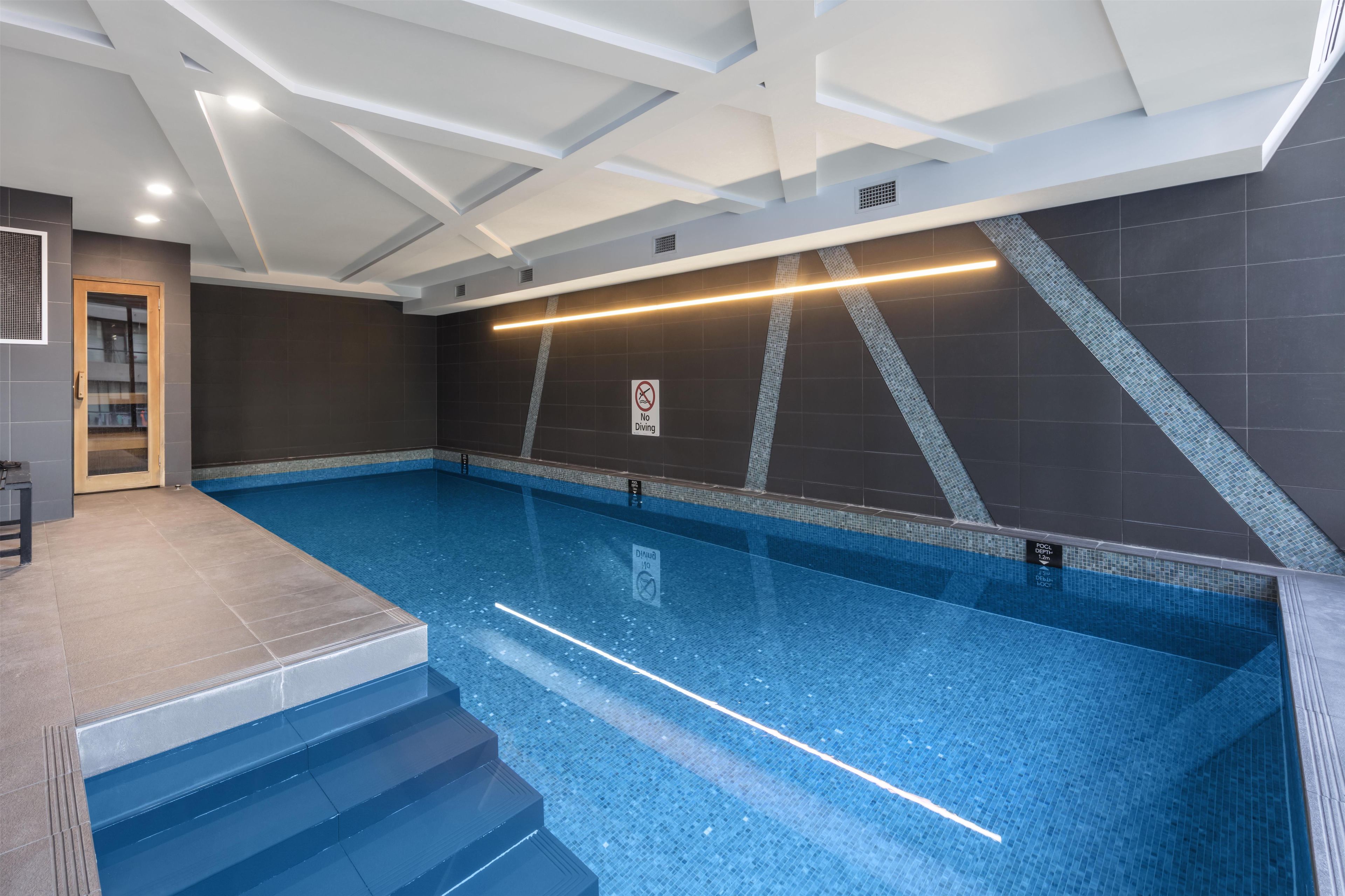 An indoor swimming pool with clear blue water, a 'No Diving' sign, and a 'No Diving' sign on the wall.