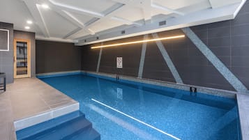 An indoor swimming pool with clear blue water, a 'No Diving' sign, and a 'No Diving' sign on the wall.