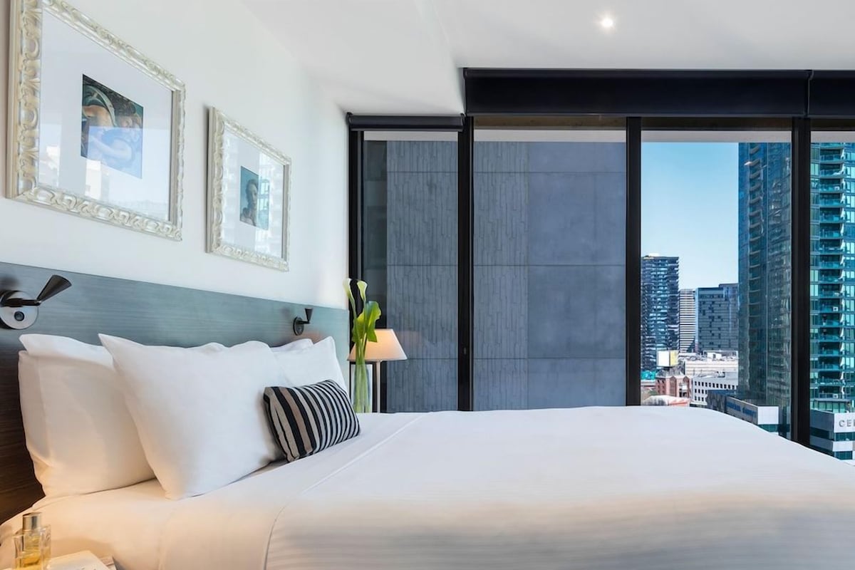 A modern hotel room with a large bed, a nightstand, a lamp, and framed pictures on the wall.