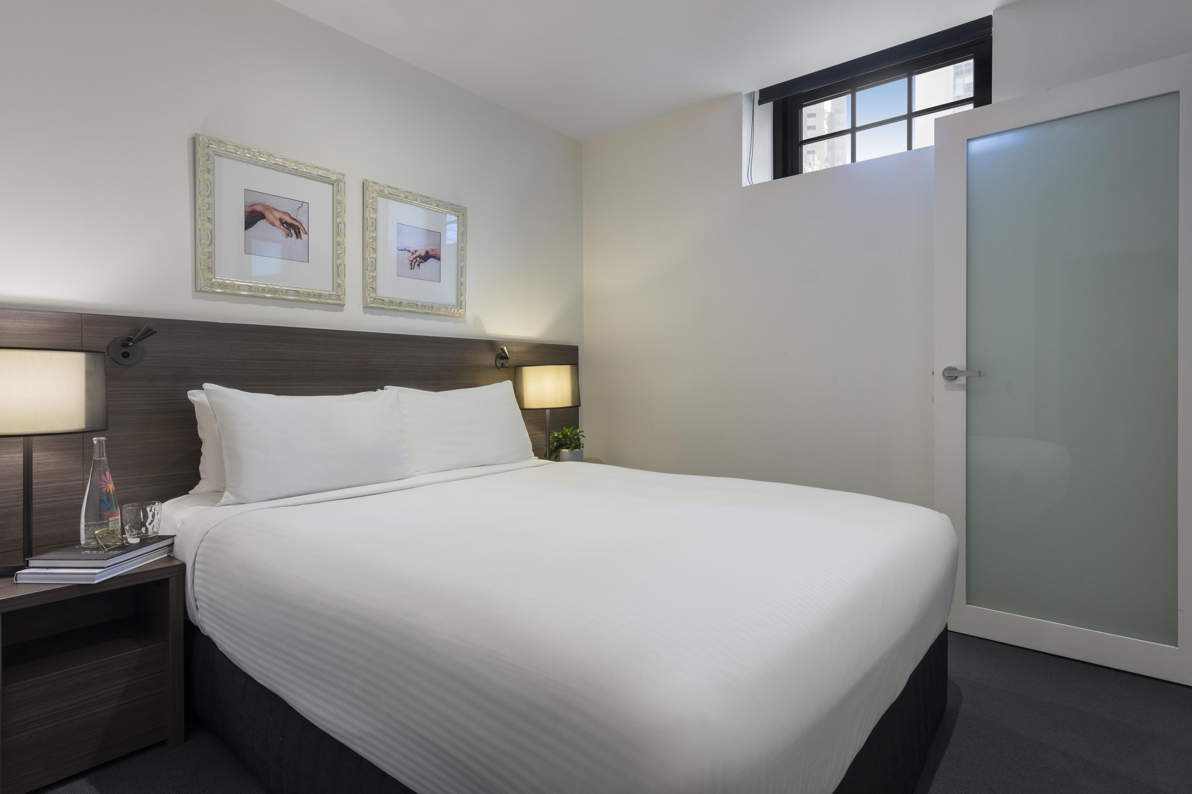 A hotel room with a bed, nightstands, a window, and a door.