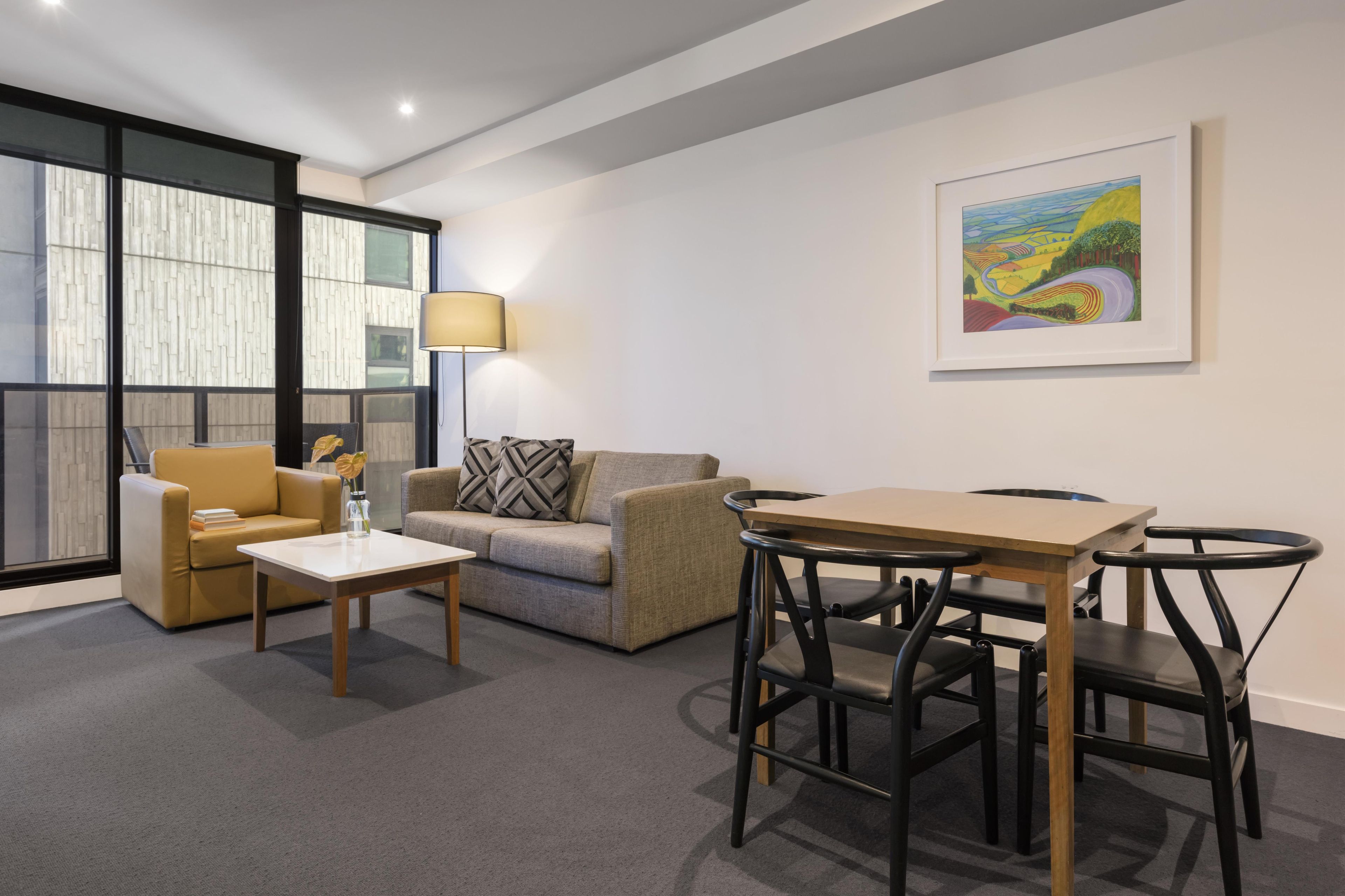 A modern living room with a sofa, a coffee table, a dining table with chairs, a lamp, and a framed painting on the wall.