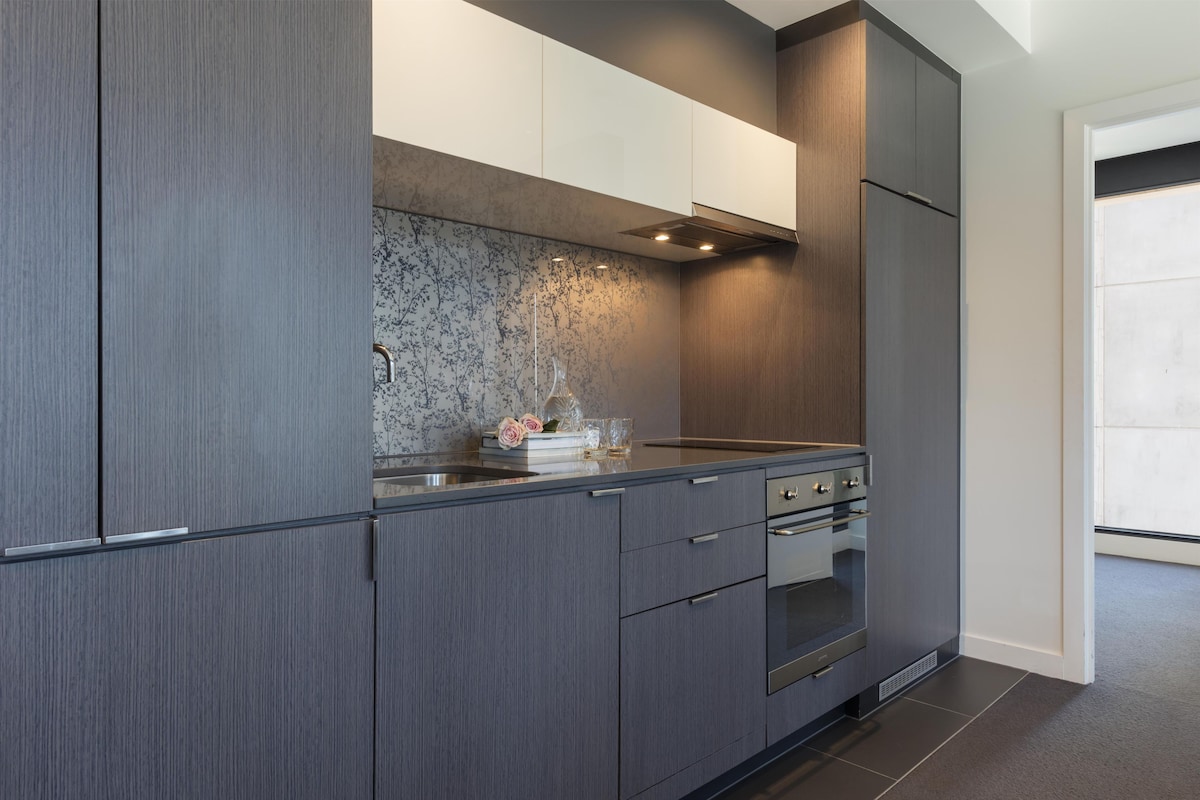 A modern kitchen with grey cabinetry, a marble backsplash, and stainless steel appliances.