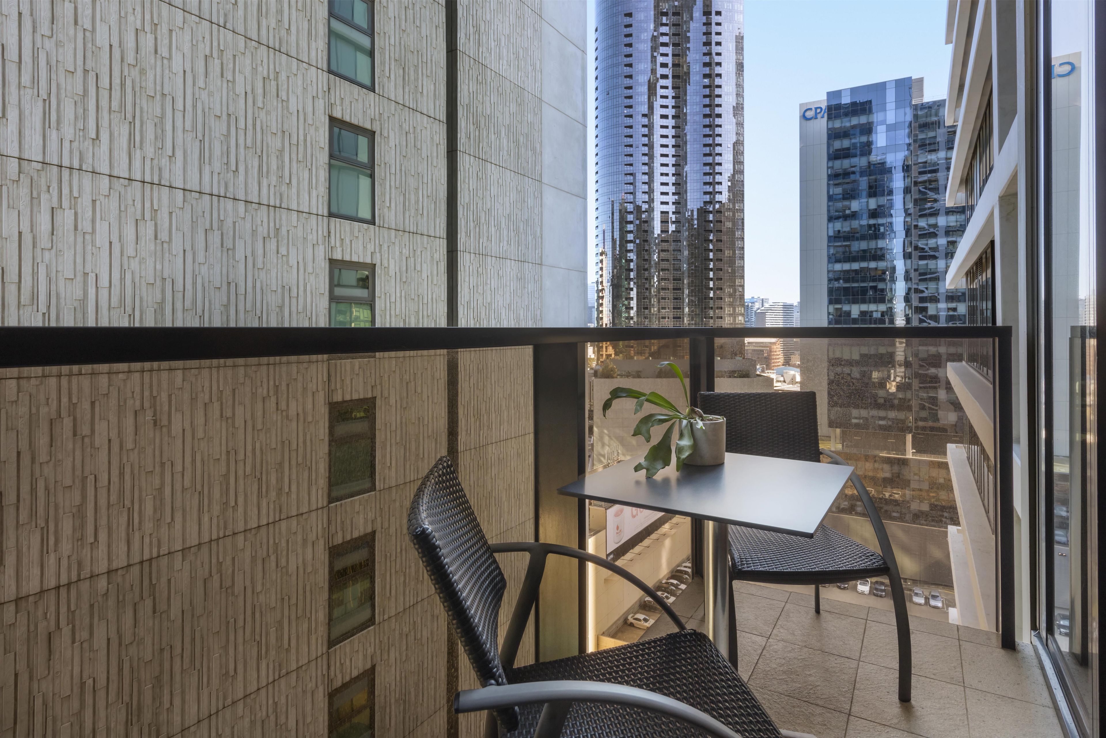 Un balcón con una mesa, sillas, una planta en maceta y vistas de edificios altos.