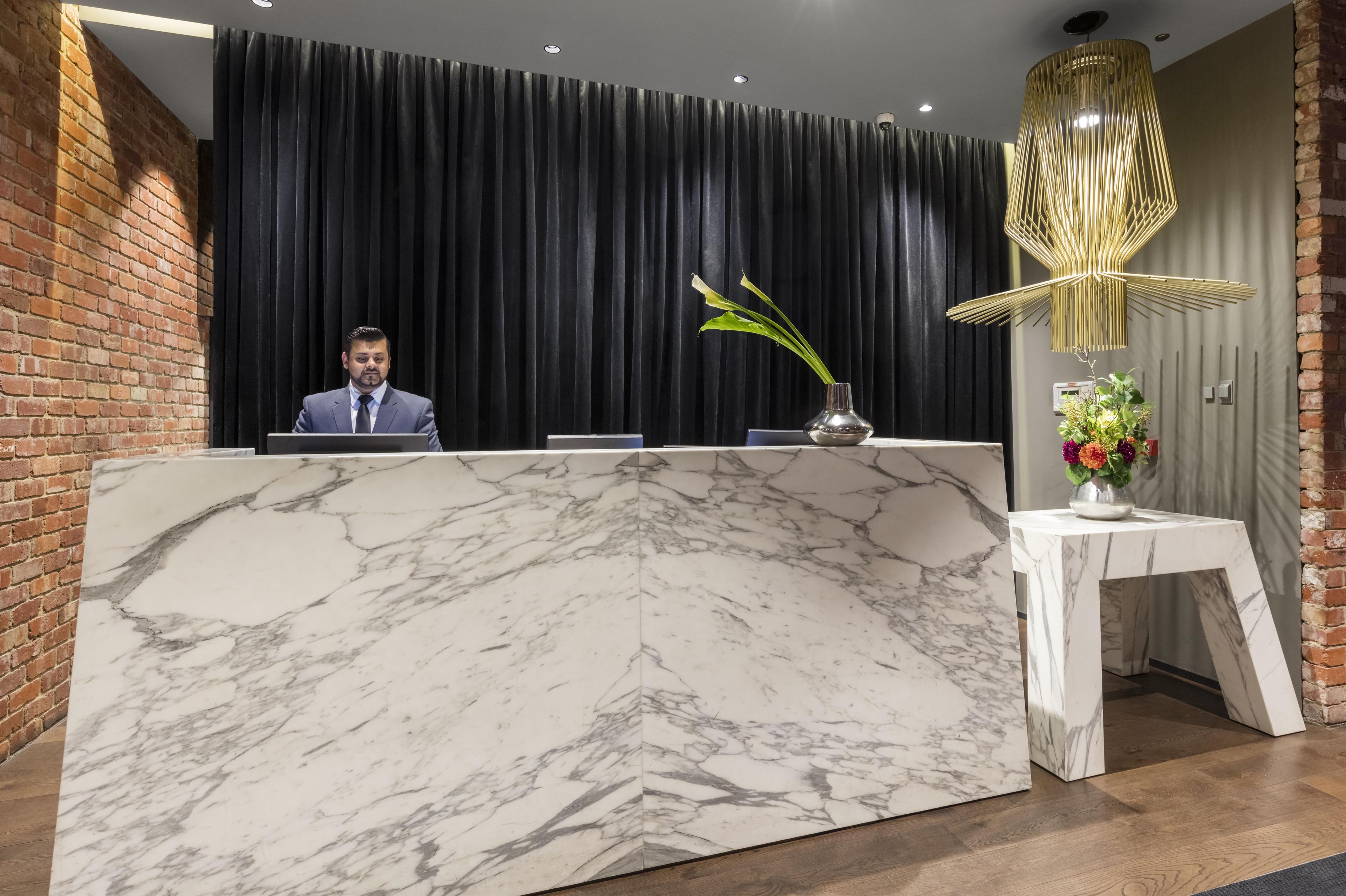 A reception desk with a marble top, a vase with flowers, and a modern light fixture.