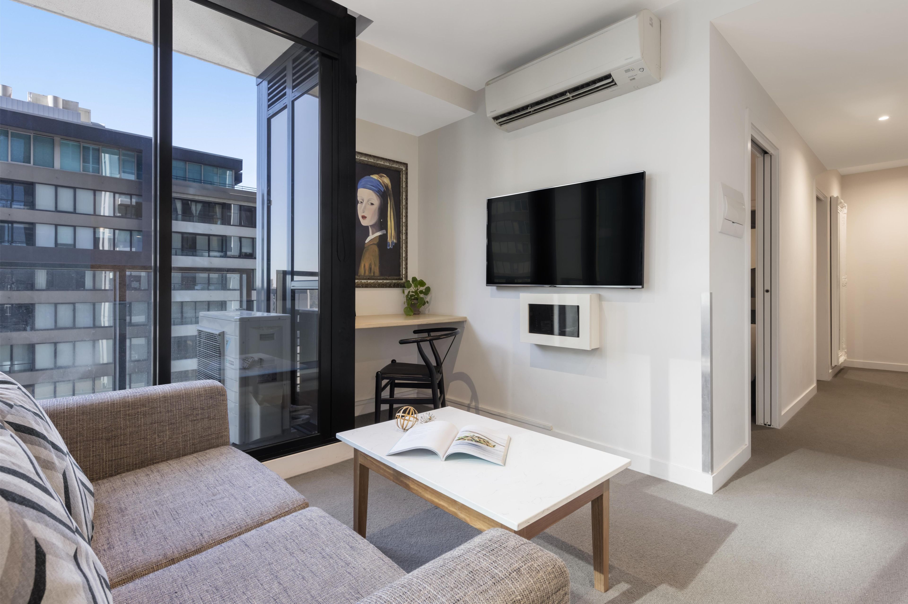 A modern living room with a sofa, a table with an open book, a mounted TV, and a painting on the wall.