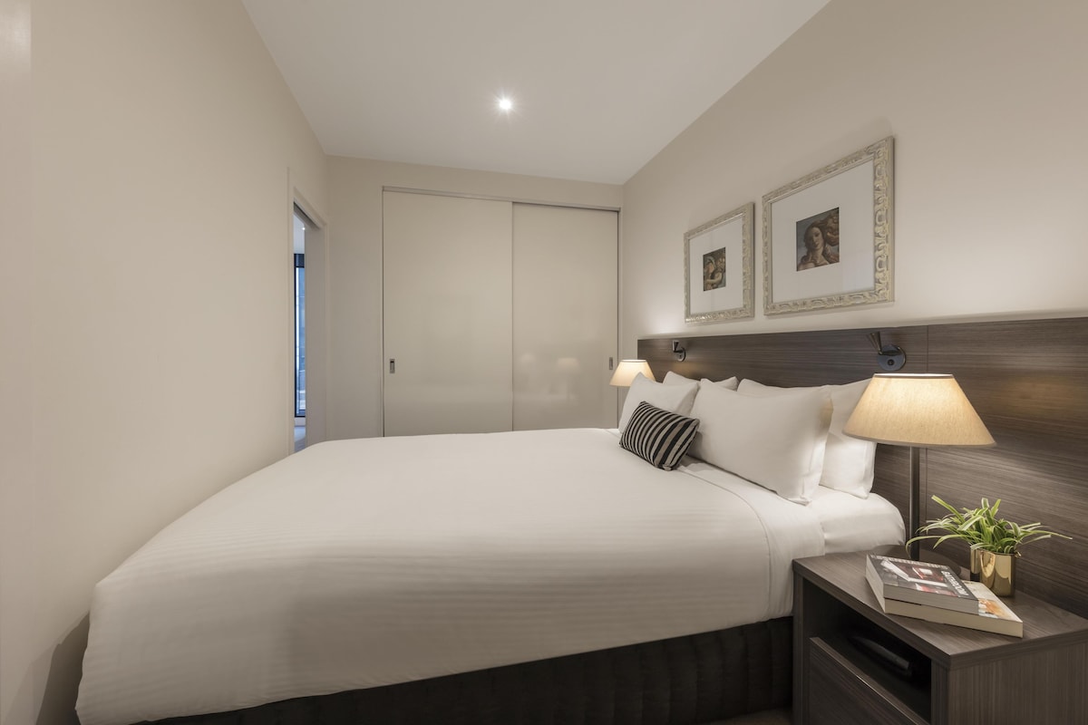 A neatly made bed with pillows, a bedside lamp, and a framed picture on the wall.