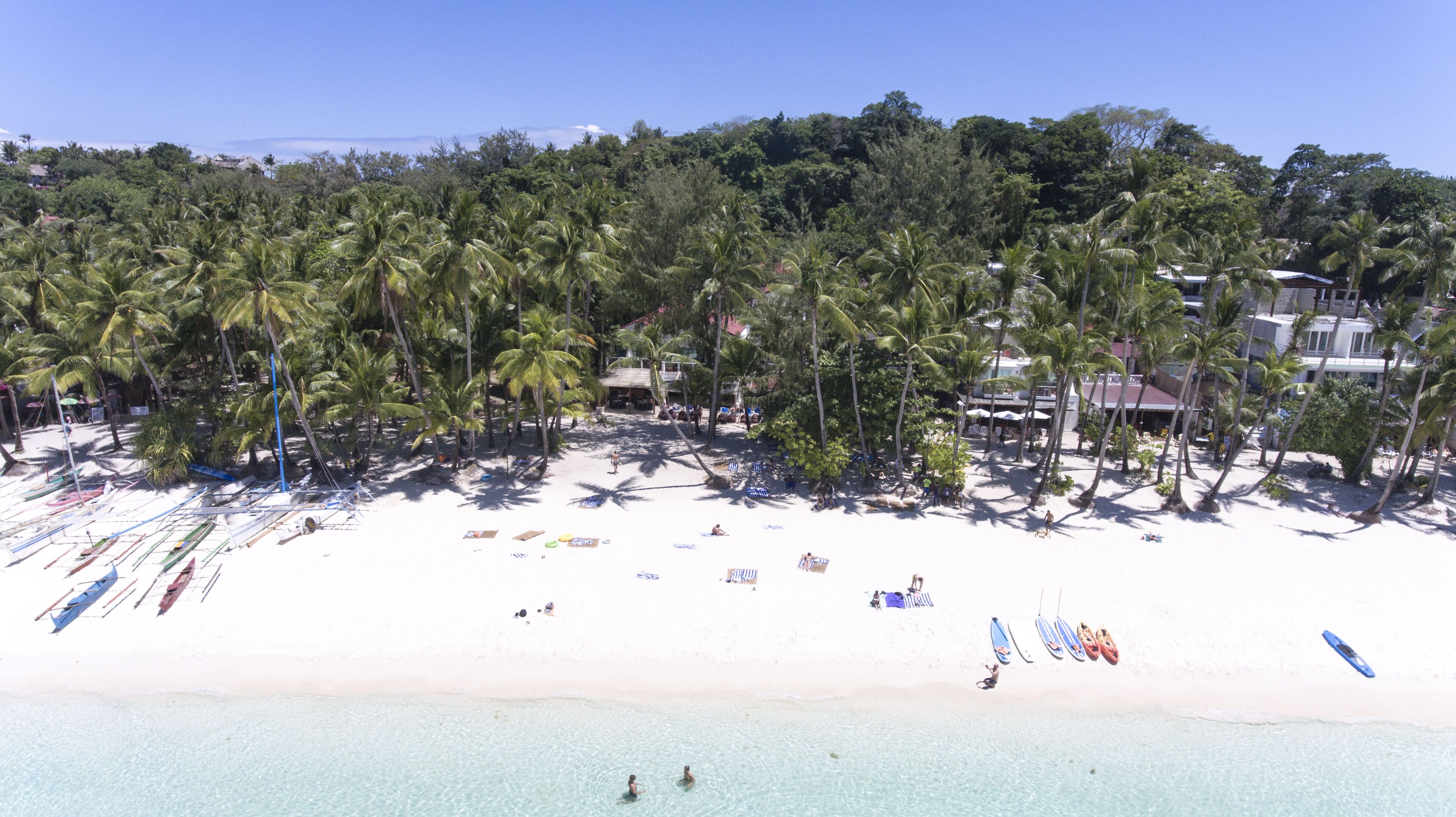 Une plage avec une eau cristalline, des palmiers et plusieurs bateaux.