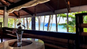 Una habitación tropical con vista al océano, una mesa redonda con un florero y muebles de madera.