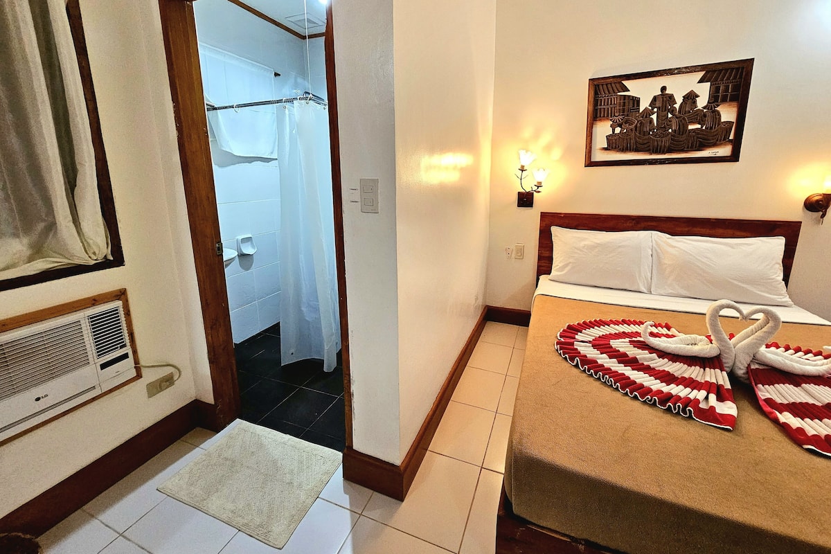 Habitación de hotel con cama, cortina de ducha, un cuadro colgado en la pared y una mesita de noche.