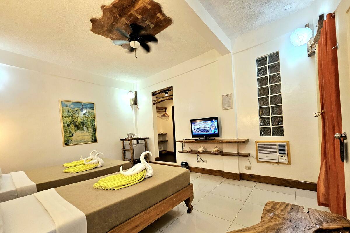 Una habitación con dos camillas de masaje, ventilador de techo, televisión y una mesa de madera.