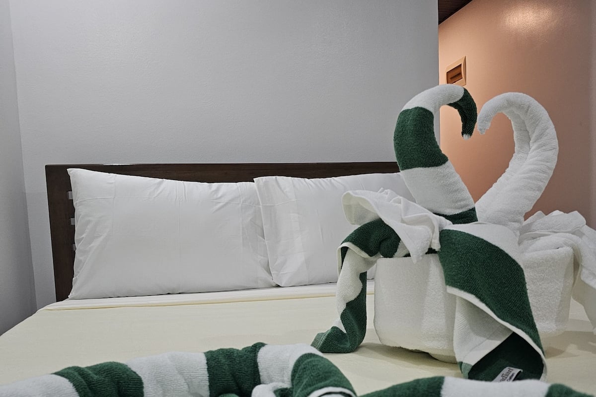 Una cama bien hecha con sábanas blancas y una manta verde y blanca a rayas.