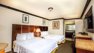 A hotel room with two beds, a desk, a chair, a television, and a bathroom visible in the background.
