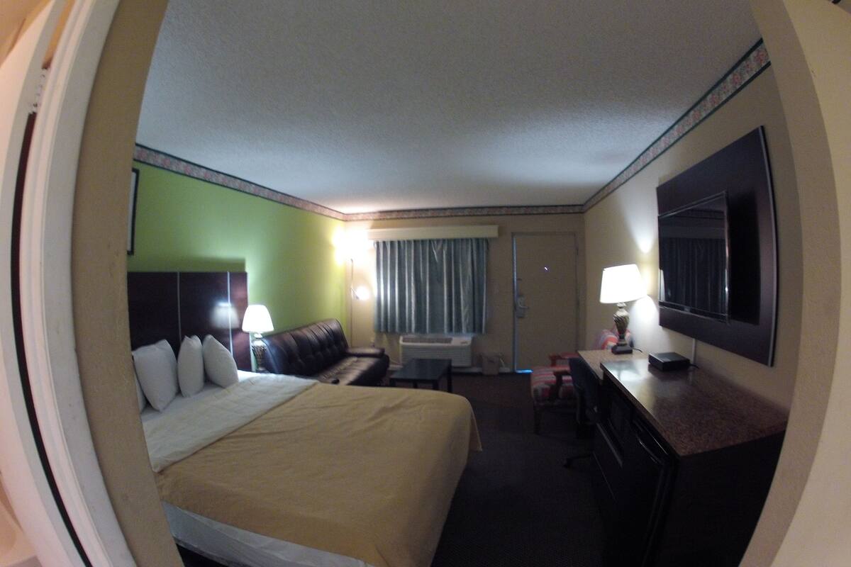 Ett hotellrum med en säng, ett skrivbord, en stol, en tv och ett fönster med gardiner.