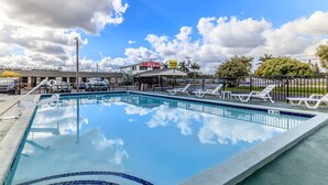 A swimming pool with a tiled edge, a fenced area with lounge chairs, and a motel sign in the background. - Budget Host Inn (Florida City)