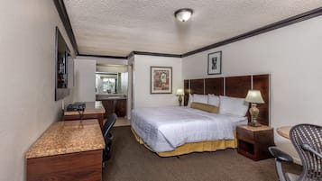 A hotel room with a bed, desk, chair, and a small kitchenette.