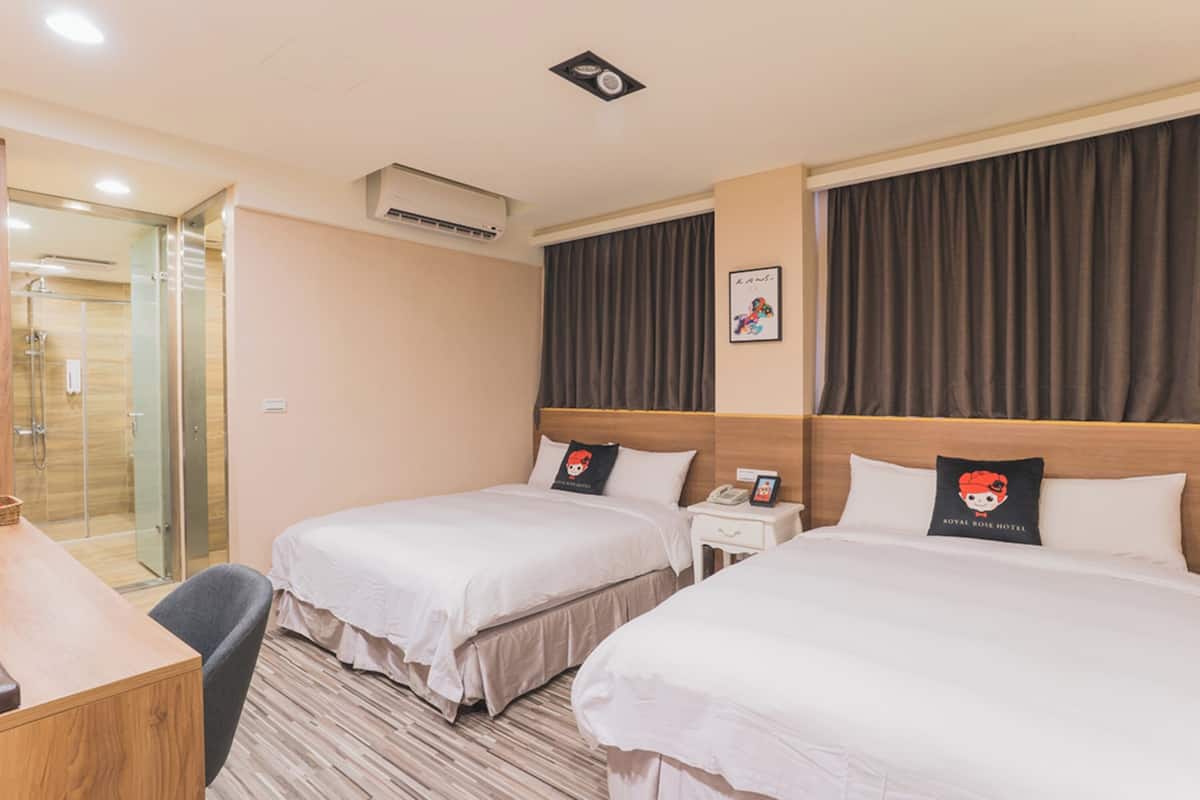 Une chambre d’hôtel avec deux lits, un bureau, une chaise, un espace douche et un tableau encadré au mur.