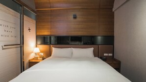 Habitación de hotel con cama, mesita de noche con lámpara, cabecero de madera y pared con un mensaje.