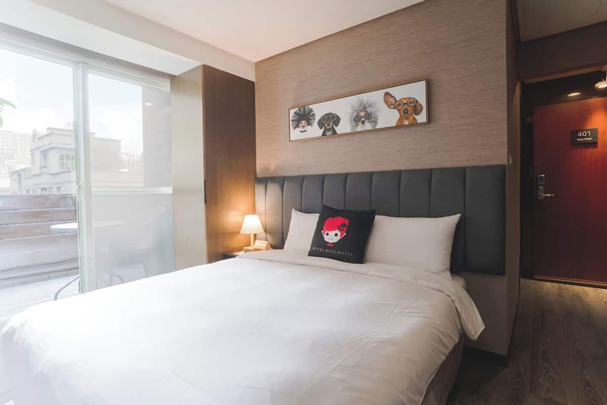 Une chambre d’hôtel avec un grand lit, une tête de lit, une fenêtre, une œuvre d’art accrochée au mur et une porte portant le numéro de la chambre.