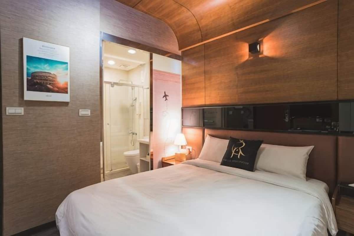 Une chambre d’hôtel comprenant un lit, une table de chevet, une lampe, un tableau encadré et un espace douche.