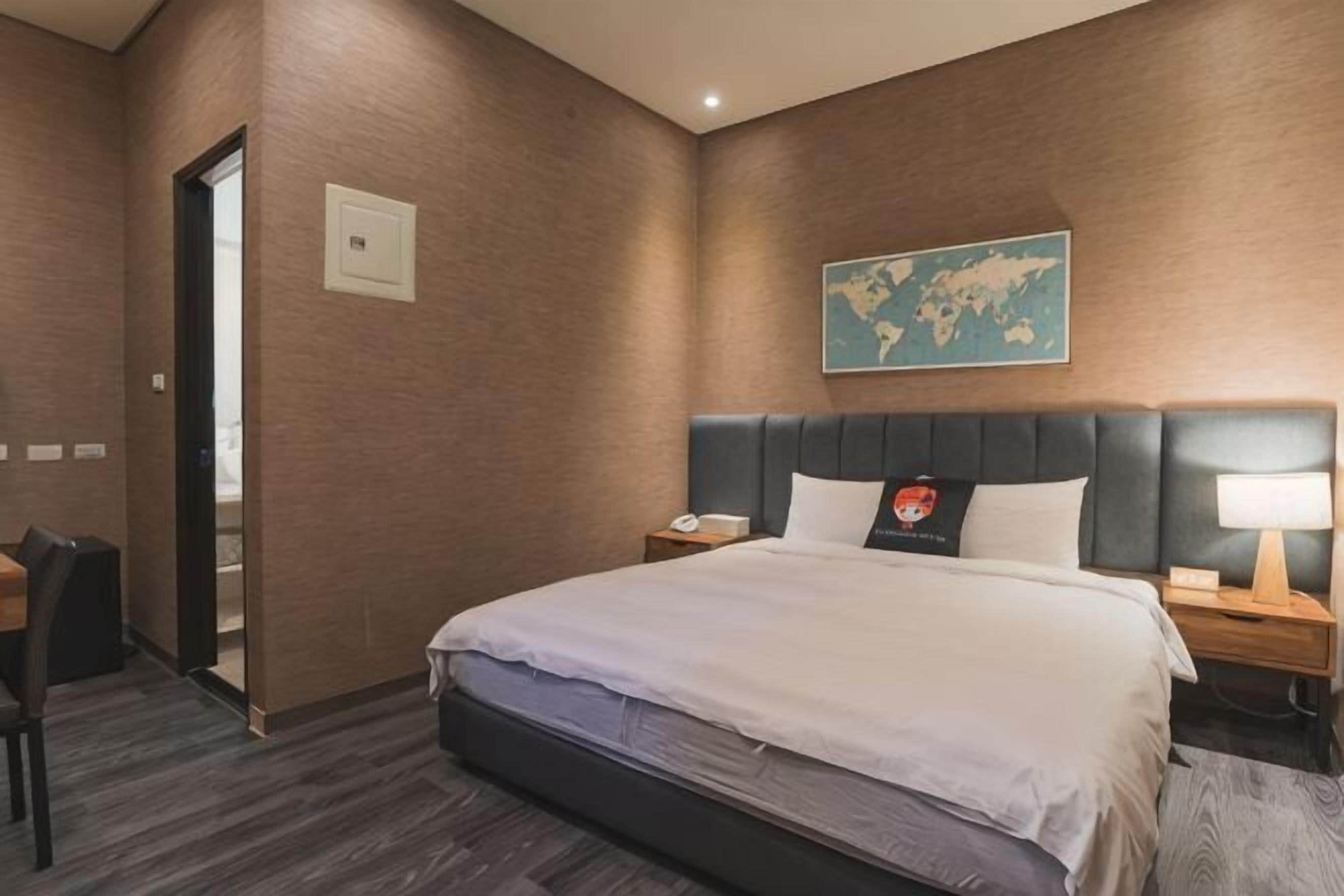 Ein Hotelzimmer mit einem großen Bett, einem Kopfteil, einem Nachttisch, einem Schreibtisch und einem Stuhl.