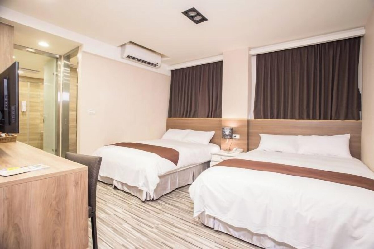 Een hotelkamer met twee bedden, een bureau, een televisie en een airconditioner.
