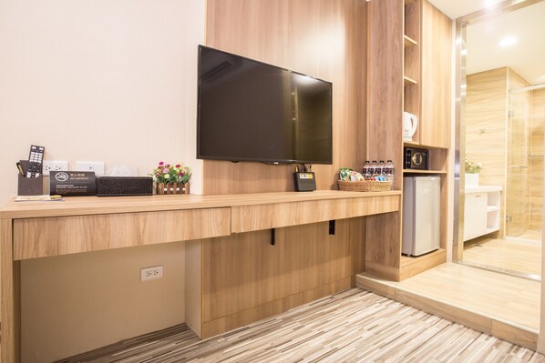 Un baño de hotel moderno con un espejo grande, un televisor de pantalla plana montado en la pared, un refrigerador pequeño y una zona de lavamanos.