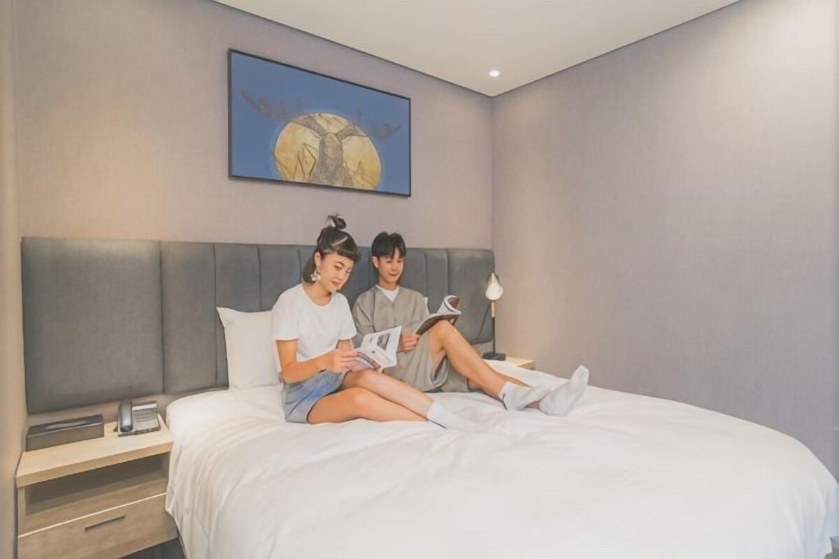 Een slaapkamer met een bed, nachtkastje, lamp en een schilderij aan de muur.