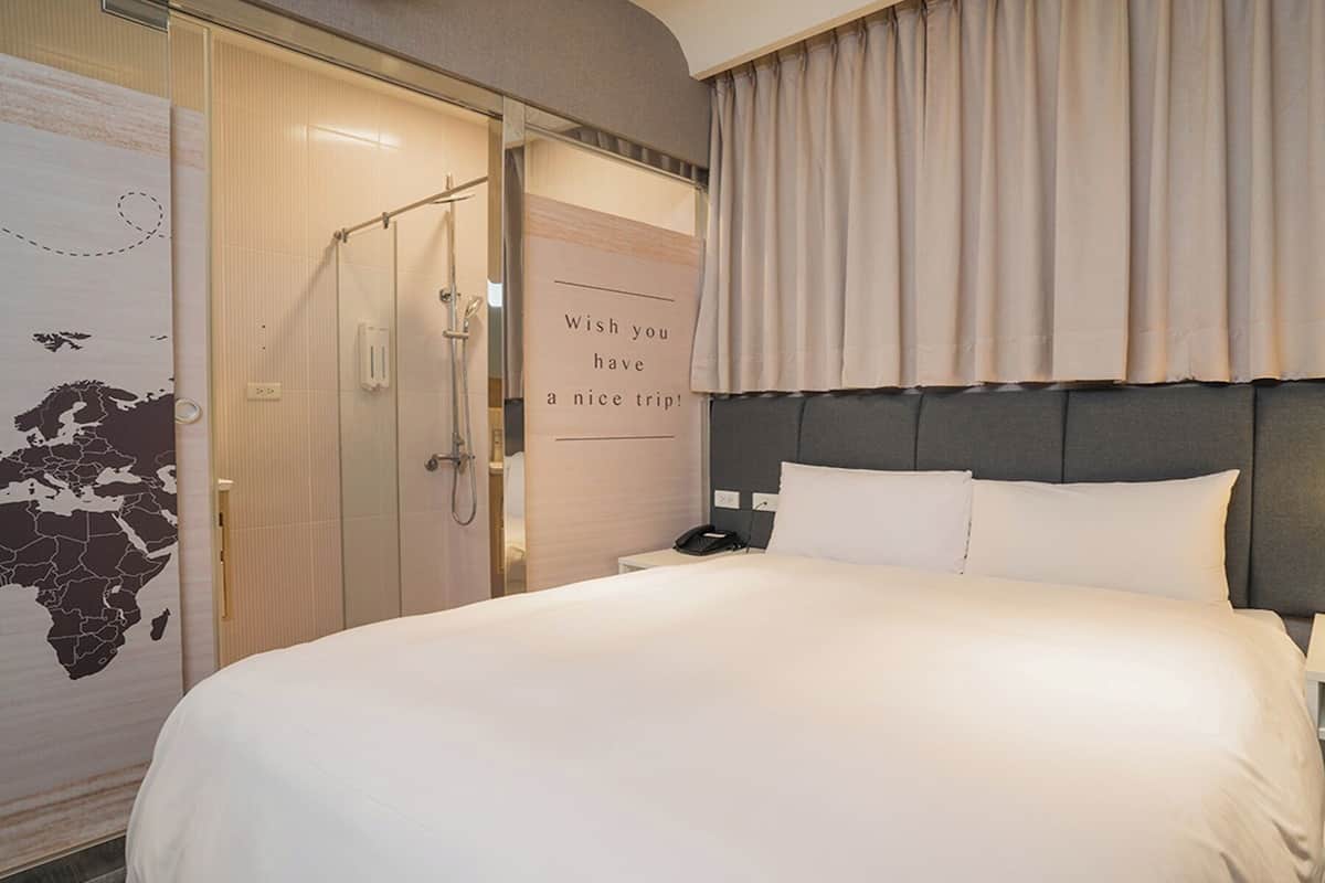 Une chambre d’hôtel avec un grand lit, une table de chevet avec une lampe, un téléphone et un espace douche.