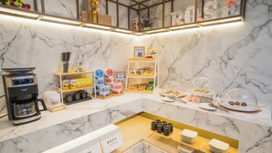 Un vestíbulo de hotel con paredes de mármol, una estación de café, estantes con aperitivos y una zona de recogida de bandejas.