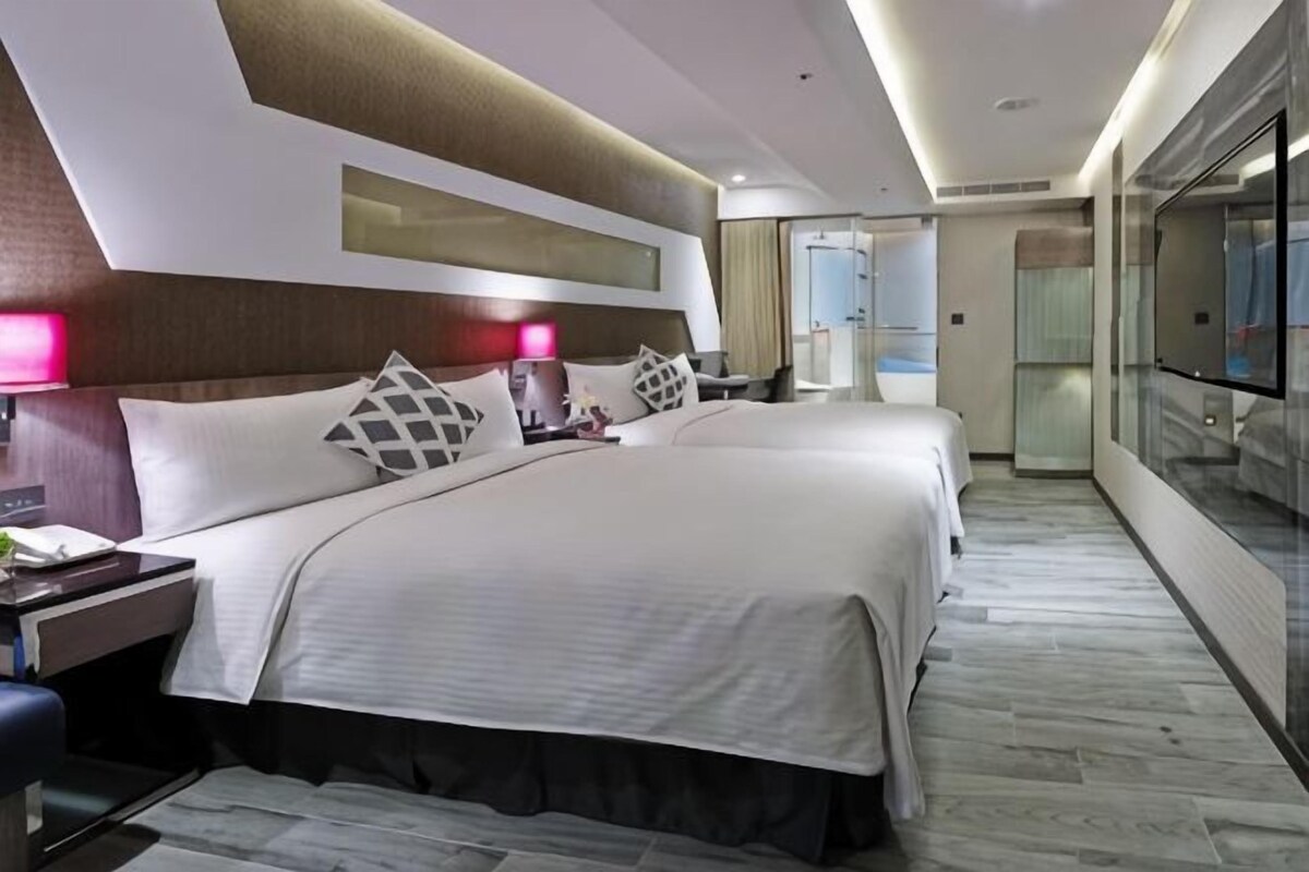 A hotel room with two beds, a desk, and a glass partition.