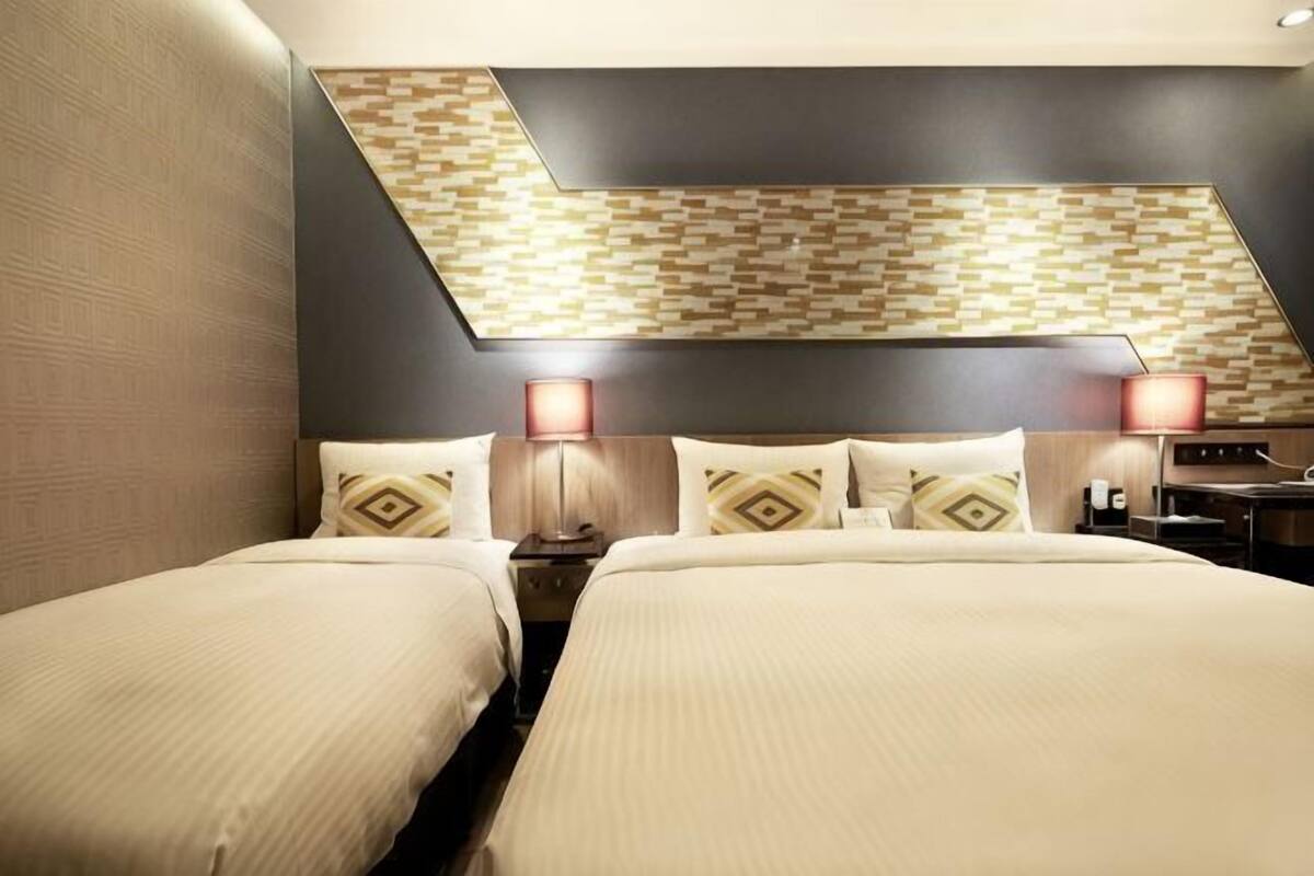 Een hotelkamer met twee bedden, een versierd plafond en twee bedlampen.