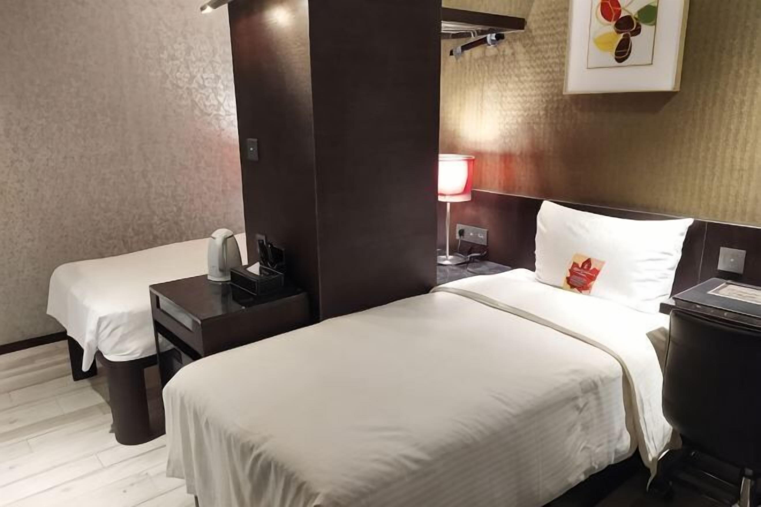 A hotel room with two single beds, a desk with a lamp, and a trash bin.