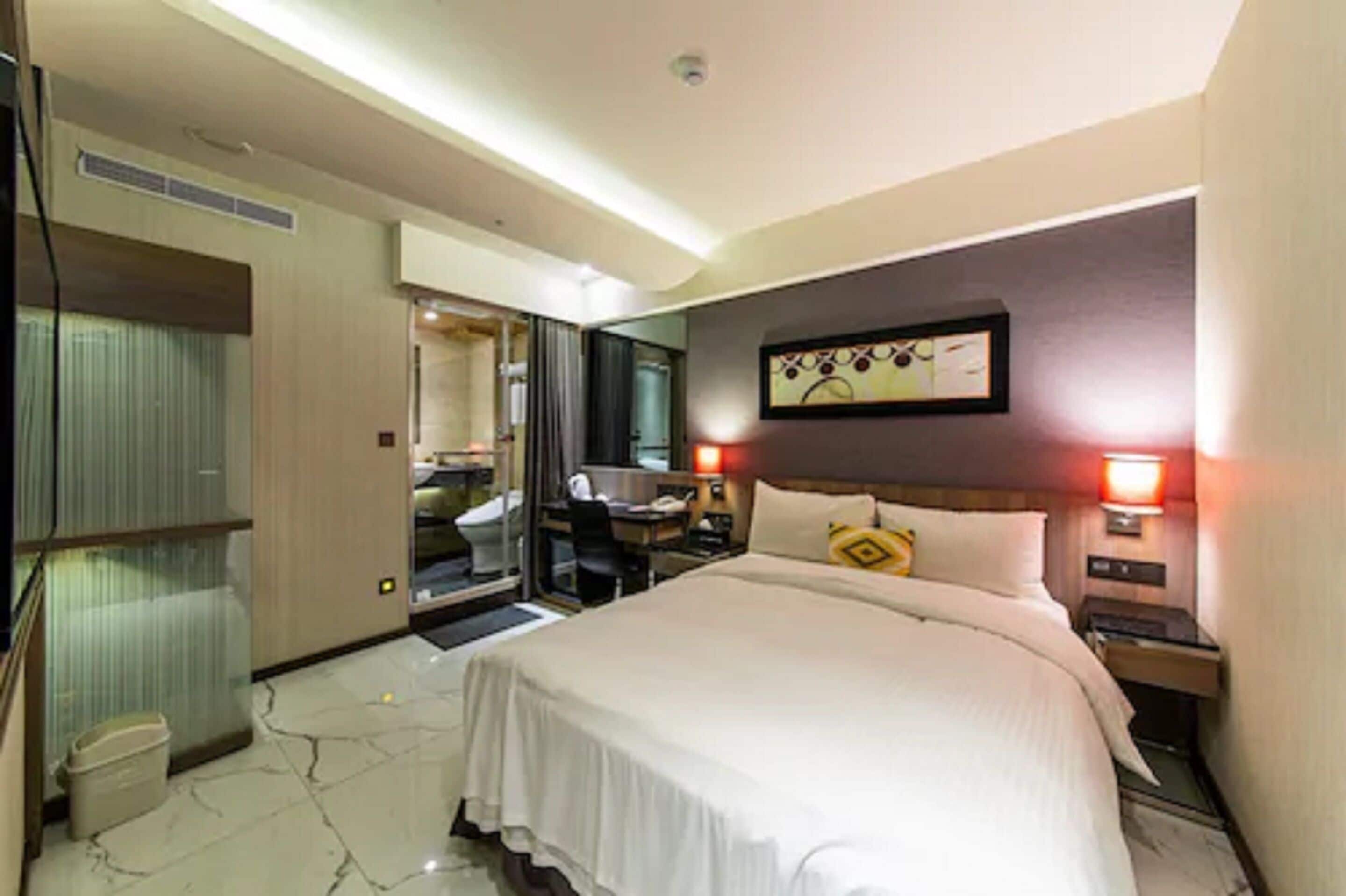 Een hotelkamer met een groot bed, een bureau met stoel, een spiegel en twee bedlampen.