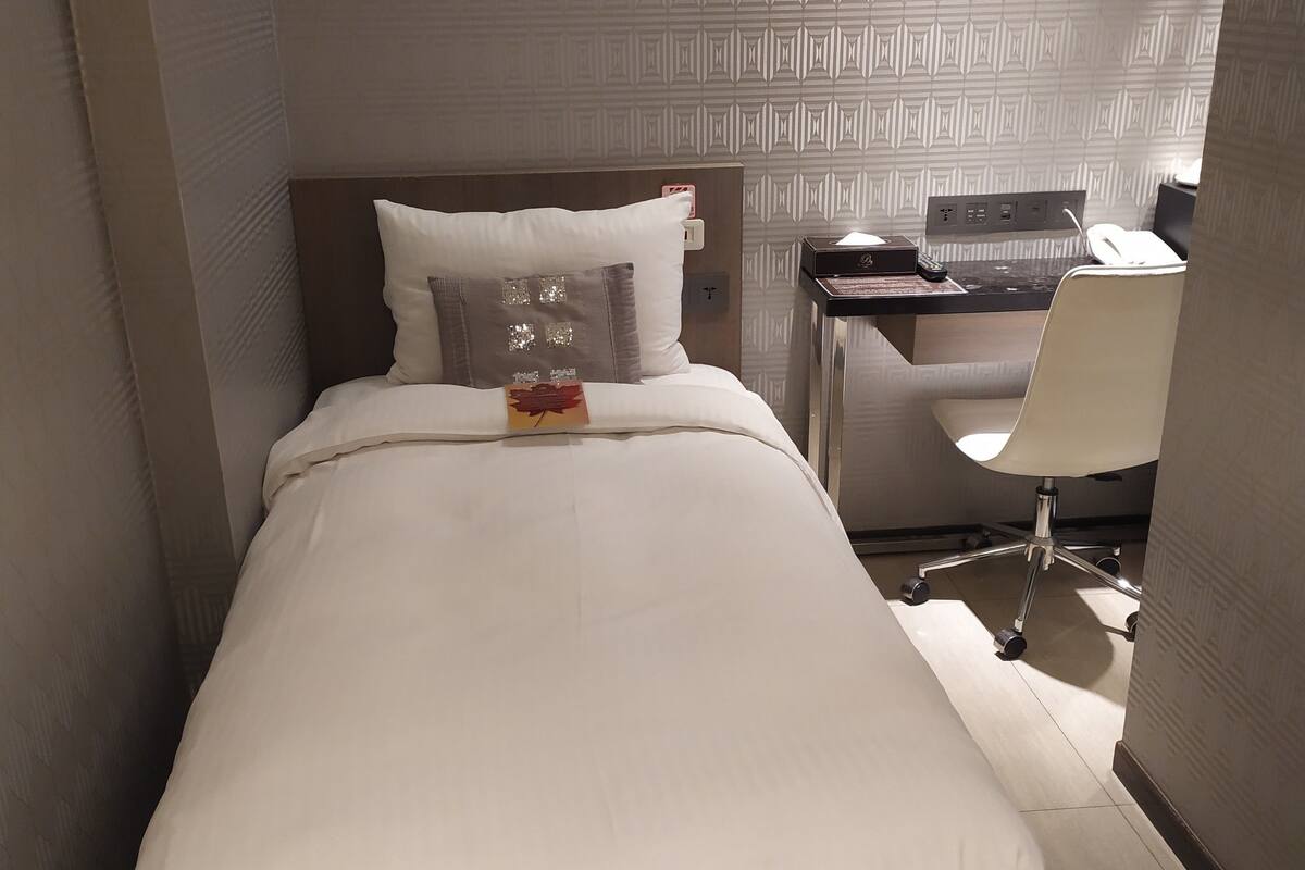 Een hotelkamer met een netjes opgemaakt bed, een bureau met stoel, en een lijst aan de muur.