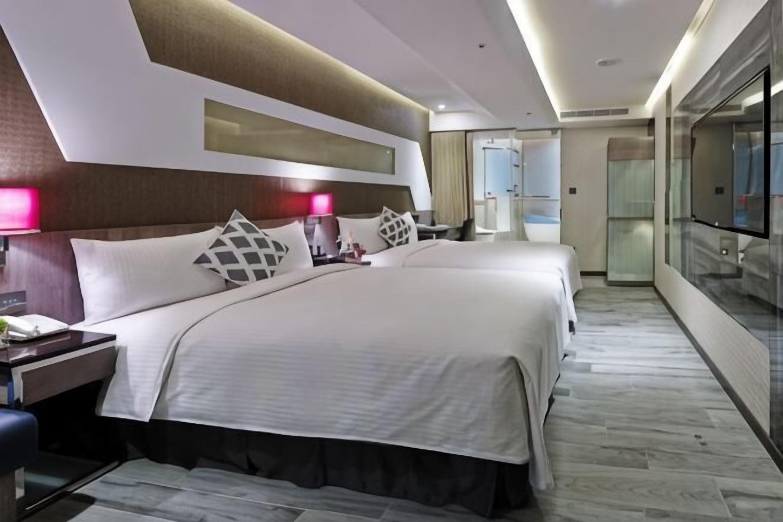 A hotel room with a large bed, bedside tables, a desk, and a glass partition.