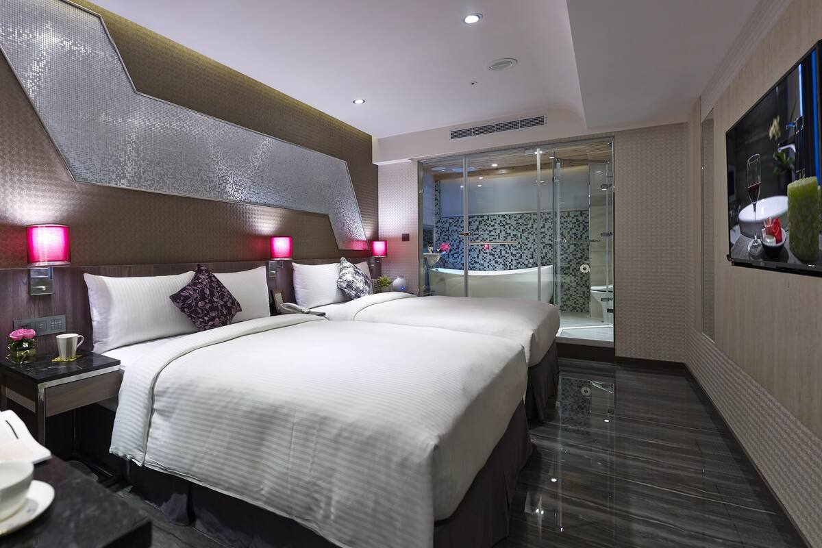 Een moderne hotelkamer met een groot bed, nachtkastjes, een douchecabine van glas en een flatscreen televisie aan de muur.