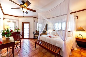 A bedroom with a bed, a ceiling fan, a bench, a desk with a lamp, and a chair.