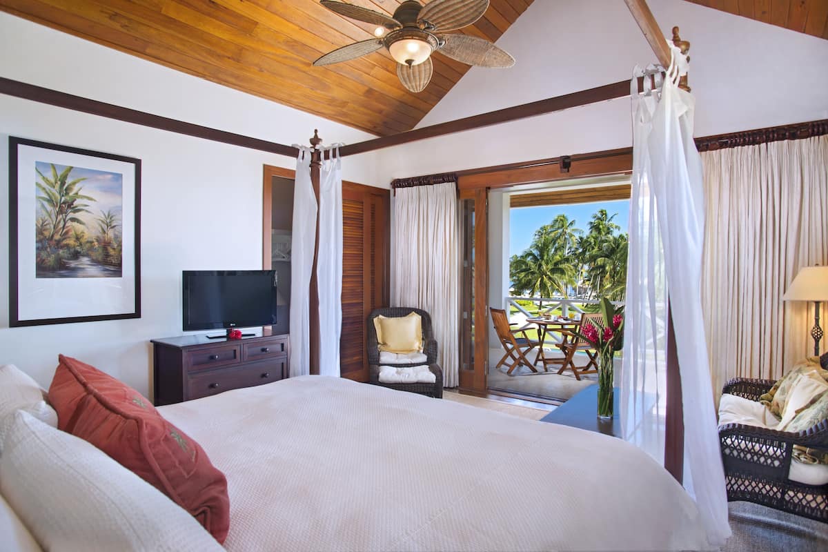 A hotel room with a large bed, a television, a chair, and a balcony with a view of palm trees.