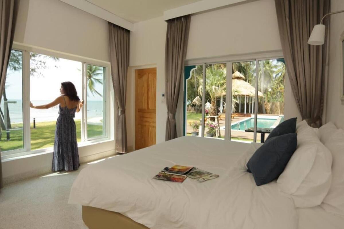 A bedroom with a large bed, a view of the ocean, and a door leading to a pool area.