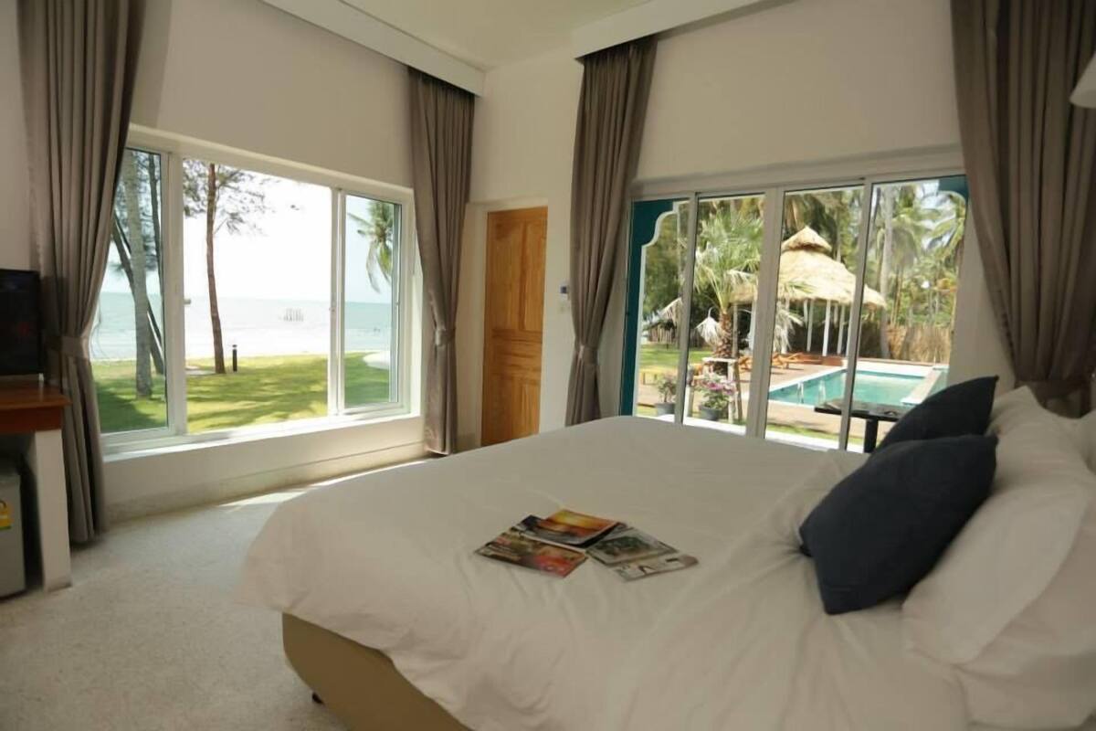 A hotel room with a large bed, a TV, and a view of a pool and tropical landscape.