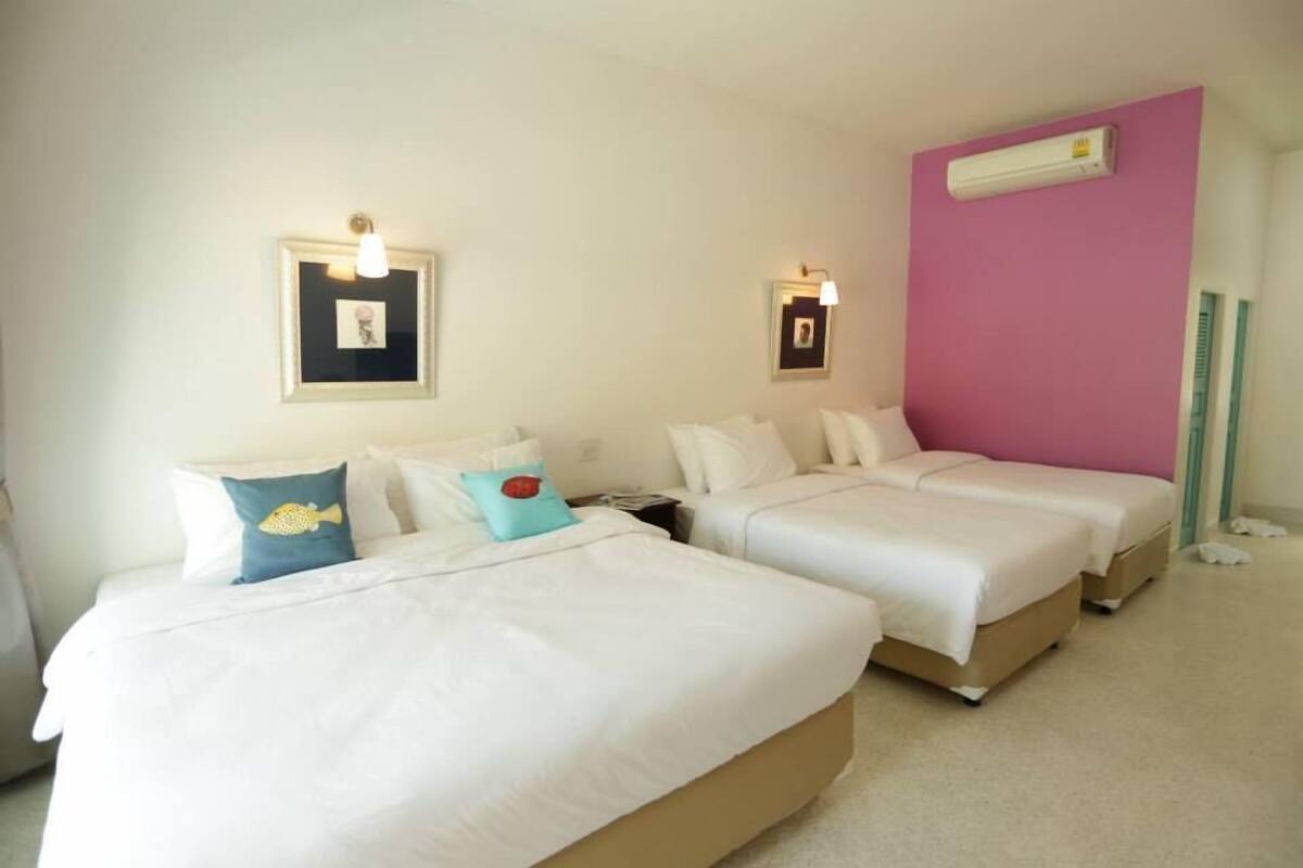 A hotel room with two single beds, a pink accent wall, and a white air conditioning unit.