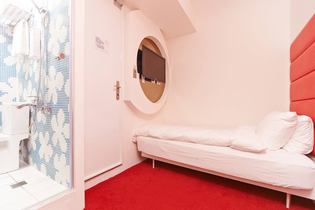 A room with a bed, a shower, and a TV mounted on the wall.
