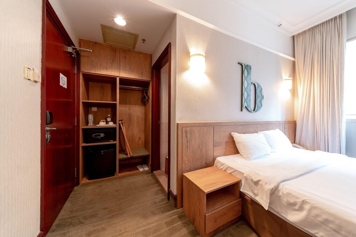 Une chambre d’hôtel avec une armoire en bois, une table de chevet, un lit avec une literie blanche et un luminaire fixé au mur.