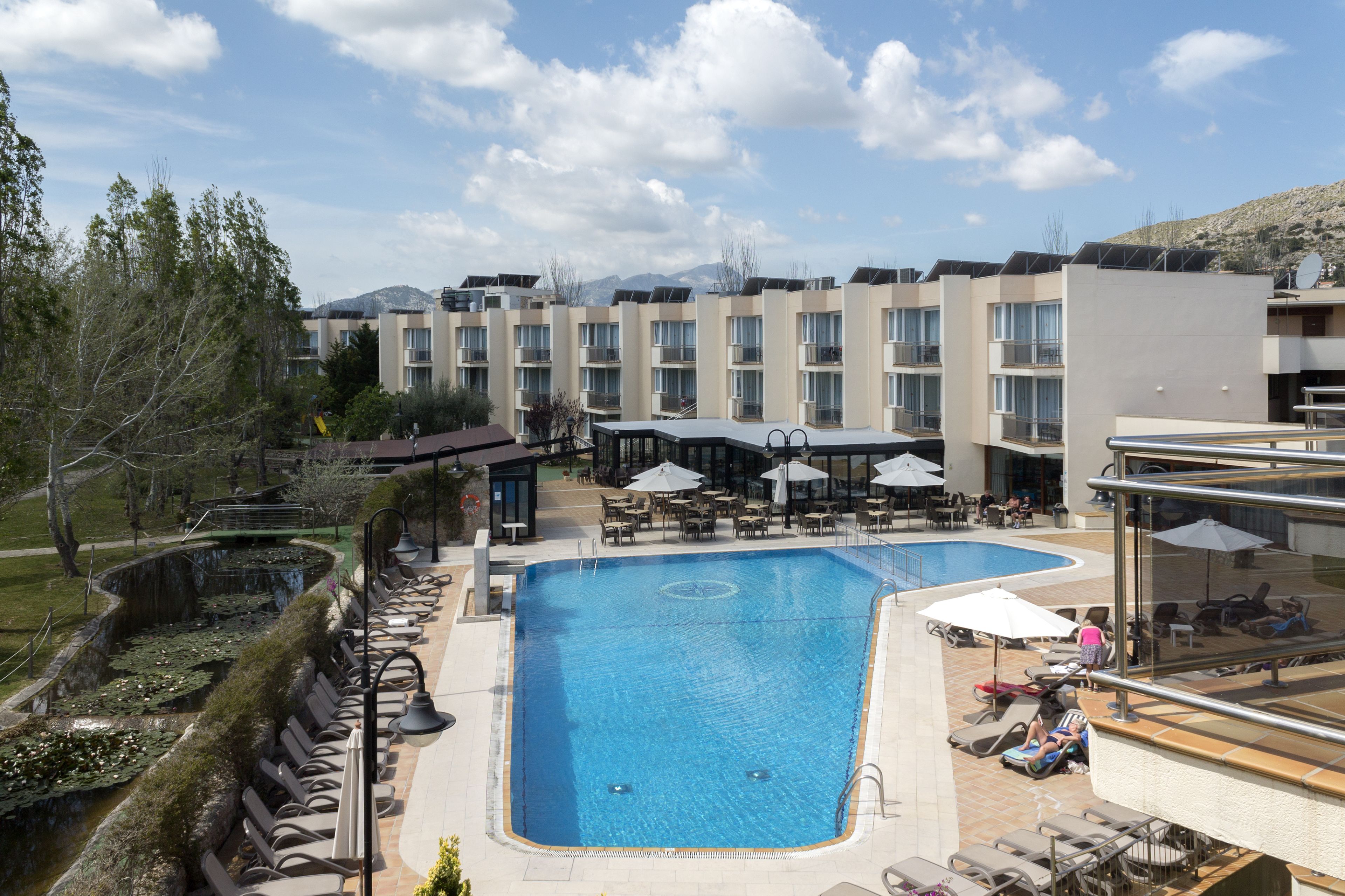 A hotel with a large outdoor swimming pool, lounge chairs, and umbrellas.