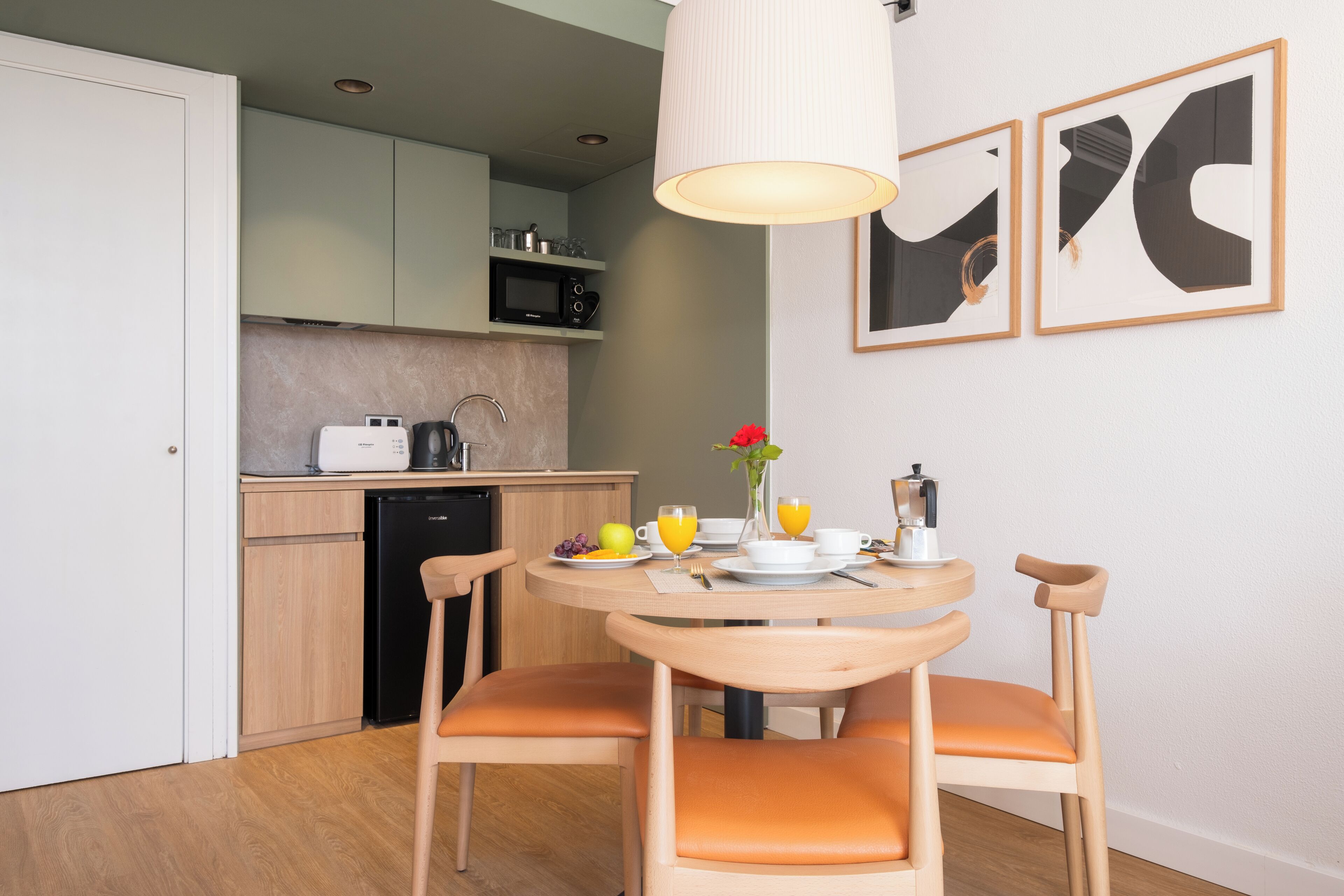 Une cuisine compacte avec un coin repas, un four à micro-ondes et un évier. Elle comprend deux chaises et une table préparée pour le petit-déjeuner.
