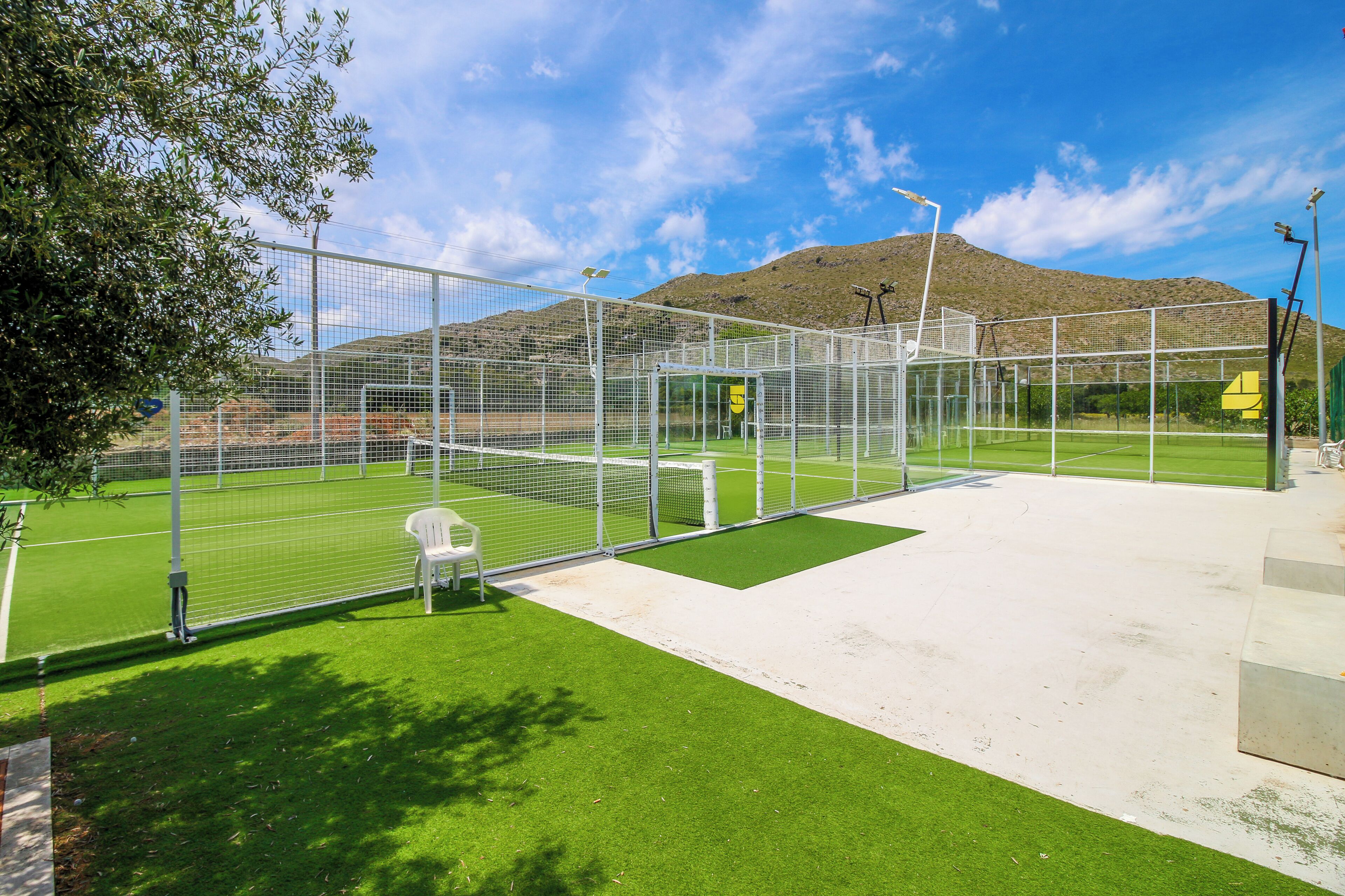 Un campo deportivo cercado con césped artificial y un arco, con montañas al fondo.